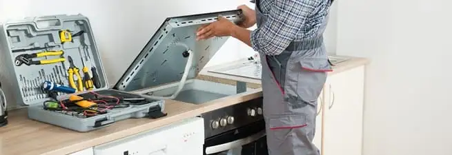 Cooktop repair technician lifting a built-in stovetop for service in Bakersfield, CA