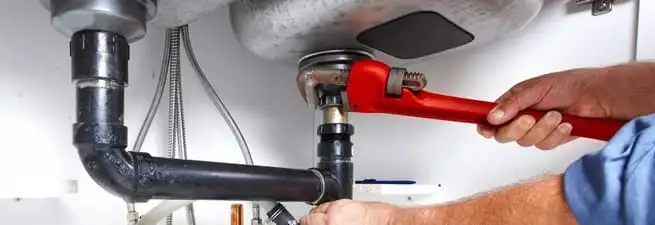 Garbage disposal repair technician tightening the sink drain and disposal connection in Bakersfield, CA