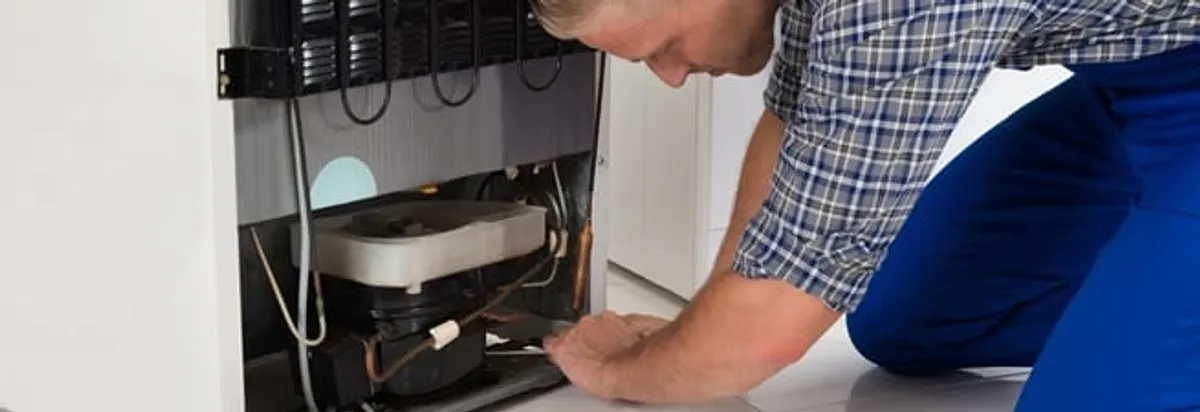 Refrigerator repair technician servicing the compressor and condenser area in Bakersfield, CA