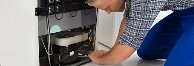 Refrigerator repair technician servicing the compressor and condenser area in Bakersfield, CA