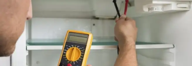 Refrigerator repair technician testing electrical components with a multimeter in Bakersfield, CA