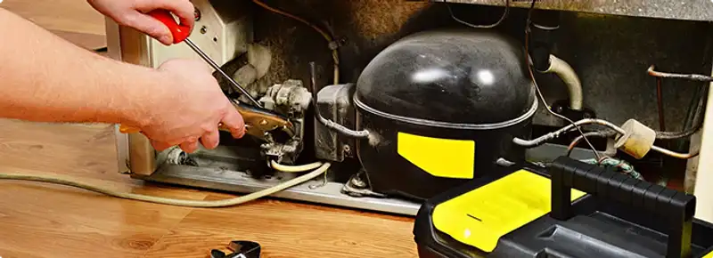 Refrigerator repair technician fixing the compressor and wiring in Bakersfield, CA